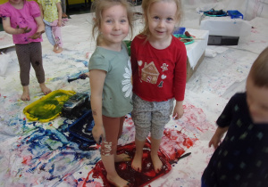 dzieci na boso na rozłożonych białych kartach papieru malują farbami