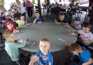 dzieci jedzą kiełbaski przy okrągłych stołach