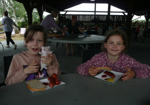 dwie dziewczynki jedzą kiłbaski przy stole