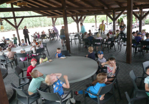 dzieci jedzą kiełbaski przy okrągłych stołach