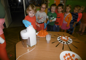 dzieci ustawione w kolejce robią sok z marchwi