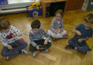 Żaczki siedząc w kole grają na instrumentach - trójkąty