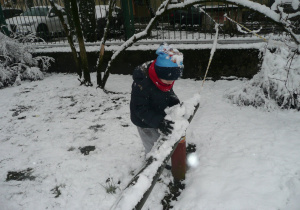 chłopiec zgarnia śnieg z drewnianej barierki