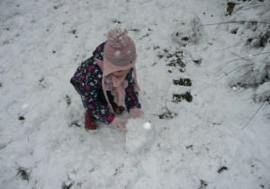 dziewczynka w różowej czapeczce podczas lepienia kuli śniegowej