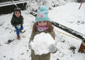 dziewczynka w niebieskiej czapeczce podczas lepienia kuli śniegowej