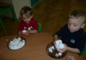 dwóch chłopców przy stoliczku lepią bałwanka ze śniegu na talerzu