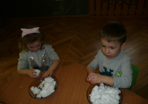 chłopczyk z dziewczynką przy stoliczku lepią bałwanka ze śniegu na talerzu