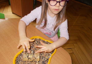 dziewczynka obtacza rolkę posmarowaną masłem orzechowym ziarenkami