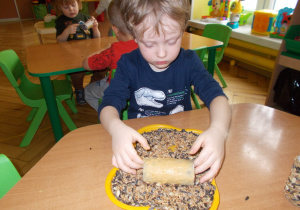 chłopiec obtacza rolkę posmarowaną masłem orzechowym ziarenkami