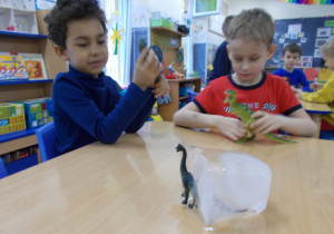 dzieci przy stolikach wydobywają z lodu figurki dinozaurów