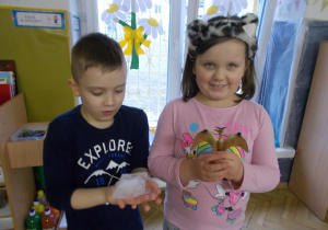 chłopczyk z dziewczynką trzymają kostke lodu i wydobytą z niego figurkę dinozaura