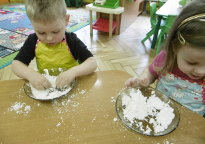 dzieci na swoich miejscach przy stoliczkach bawią się przygotowanym wcześniej sztucznym śniegiem