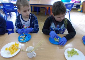 dzieci przy stoliczkach nakładają na wykałaczki owoce