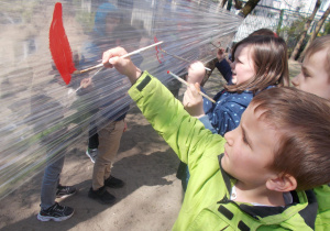 Juniorzy malują farbami na folii zawieszonej w ogrodzie przedszkolnym