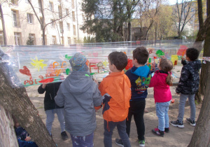 Juniorzy malują farbami na folii zawieszonej w ogrodzie przedszkolnym