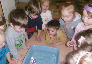 dzieci różnymi sposobami próbują umeiscowić papierową łódkę w drugim końcu miski