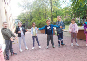 Juniorzy w przygotowaniach do występu z okazji Dnia Mamy i Taty w ogrodzie przedszkolnym ustawieni w półkolu