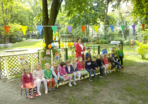 Żaczki na ławeczce w ogrodzie przedszkolnym w oczekiwaniu na atrakcje związane z Dniem Dziecka