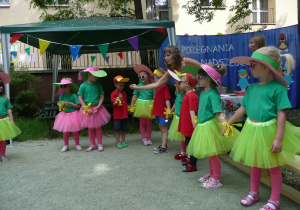 Smyki ubrane w kolorowe spódniczki i bluzeczki prezentują wiersze i piosenki z okazji zakończenia roku szkonego