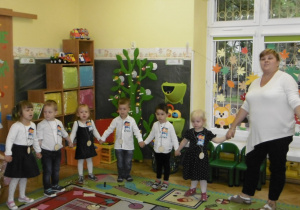 Pasowane na Przedszkolaków dzieci ustawione w półkolu śpiewaja piosenkę