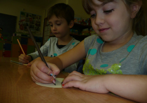 dziewczynka z chłopcem przy stoliku rysują kredkami ołówkowymi