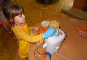 dziewczynka w fartuszku i rękawiczkach przygotowuje sok marchowkowy