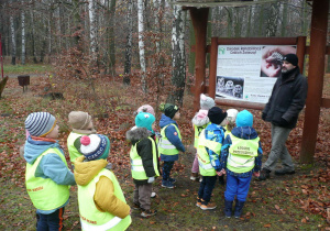 Smyki w Lesie Łagiewnickim wysłuchuja opowiadanie przy tablicy informacyjnej