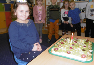 dziewczynka w czapeczce urodzinowej przed tortem