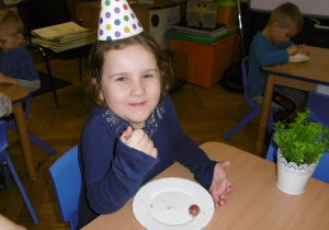 dziewczynka w czapeczce urodzinowej zjada tort urodzinowy