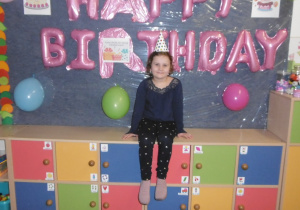 dziewczynka w czapeczce urodzinowej na tle dekoracji urodzinowej