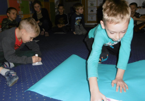 Juniorzy na dywanie przyklajają przygotowane wcześniej obrazki