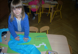 dziewczynka przy stoliczku przygotowuje pracę plastyczną na konkurs