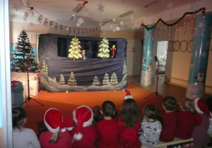 dzieci ubrane na czerwono oglądają teatrzyk pt. "Zimowa opowieść"