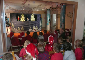 dzieci ubrane na czerwono oglądają teatrzyk pt. "Zimowa opowieść"