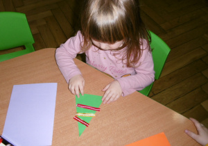 dziewczynka przy stoliku wykonuje świąteczną kartkę
