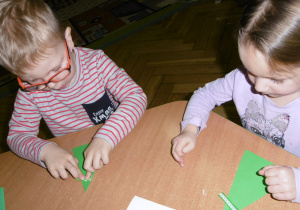dwoje dzieci przy stoliku wykonuje świąteczną kartkę