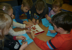 Juniorzy przy stoliczkach wykonują kartki z Iskierkami Emocji dla dzieci ze Szczecina