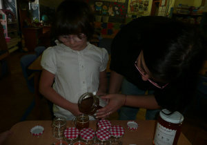 dziewczynka nalewa miód do słoiczka