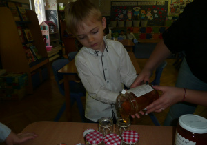 chłopczyk nalewa miód do słoiczka