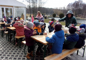 Juniorzy siedzą przy drewnianych ławeczkach popijając ciepłą cherbatę