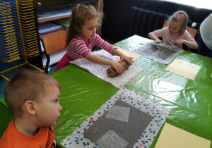 dzieci siedzą przy stole i układją elementy na swoich projektach