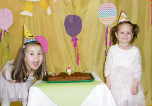 dziewczynki solenizantki przy torcie w urodzinowych czapeczkach na głowach