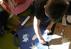 dzieci przyklejają na sylwecie garnka symbole wiosny