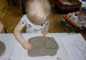 dziewczynka odrysowuje kształt serca na przygotowanej wcześniej glinie