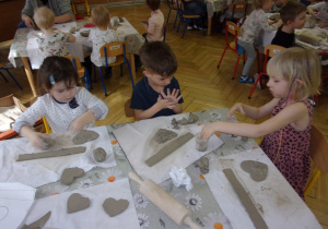 dzieci przy stoliczkach wycinają z gliny wcześniej odrysowany kształt serca