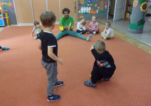 Żaczki siedzą w kole podczas zajęć Capoeira, dwoje dzieci w środku koła wykonuje ćwiczenie w parze