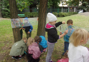 Juniorzy malują na foli owiniętej wokół drzew w ogrodzie przedszkolnym