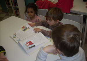 dzieci w bibliotece oglądają książki przy stoliczkach