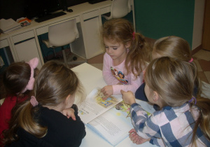 dzieci w bibliotece oglądają książki przy stoliczkach