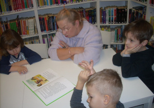ciocia Beatka czyta dzeciom książkę przy stoliku w bibliotece